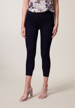 Marineblauwe skinny jeans van denim met een halflange taille en vijf-pocket ontwerp, gecombineerd met lichtpaarse strappy hakken.