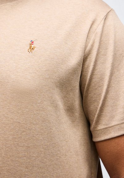 Μπεζ κοντομάνικη πουκάμισο με μικρό κεντημένο λογότυπο παίκτη πόλο πάνω σε άλογο στο αριστερό στήθος.