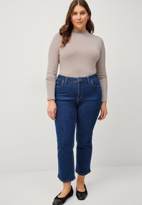 Donkerblauwe denim jeans met een hoge taille, rechte snit en enkel lengte. Gecombineerd met een lichtbeige, aangesloten top met lange mouwen.