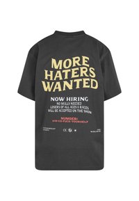 Černé bavlněné tričko s výrazným žlutým a červeným potiskem na zádech, včetně nápisu "Více nenávistníků žádáno" a dalších informací o přijímání.