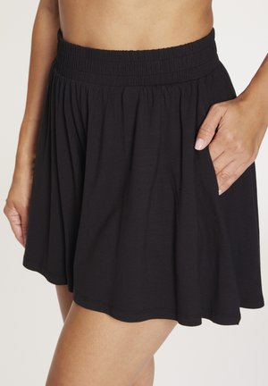 Black flowy skirt with an elastic waistband worn mid-thigh, with a hand tucked into the right side pocket.