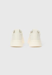 Bijele tenisice od glatke kože, okruglog vrha i robusne, kremaste potplate. Imaju petnu petlju za jednostavno obuvanje.