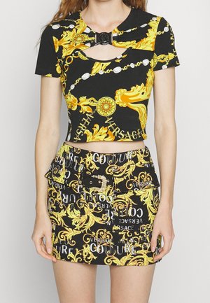 Czarny crop top i mini spódniczka z żółtymi i białymi barokowymi wzorami i tekstem, z przednią klamrą i krótkimi rękawami.