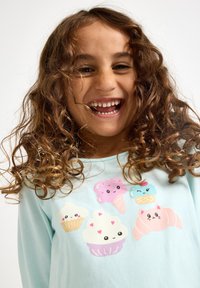 Camicia a maniche lunghe azzurro chiaro con illustrazioni giocose di cupcake e coni gelato in colori pastello delicati. Tessuto morbido al tatto.