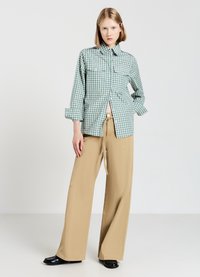 Green and white checked button-up shirt with two chest pockets, paired with light beige wide-leg trousers and black shoes.
