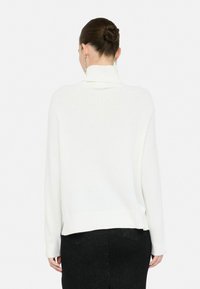 Maglione bianco a collo alto in maglia con orlo e polsini a coste, dalla vestibilità rilassata, dotato di un design a collo alto nella parte posteriore e dettagli minimalisti.