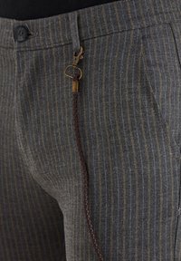 Grau gestreifte Hose mit einem gewebten Detail aus braunem Leder und einem bronzefarbenen Akzent an der Taille. Verfügt über einen standardmäßigen Knopfverschluss und Taschen.