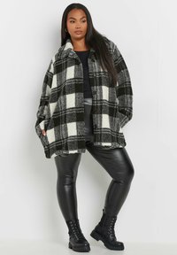 Svart och vit rutad oversized fleecejacka med framskjutna knappar, sidofickor, bärs över en svart topp och ihop med svarta leggings och stövlar.