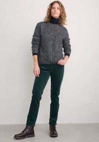 Szary sweter z dzianiny z wzorem w warkocz, granatowy golf, zielone spodnie z kordurowej tkaniny oraz ciemnobrązowe buty sznurowane. Prosty, fakturowany i dopasowany design.