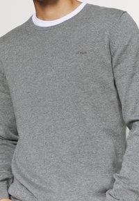 Grau gestrickter Pullover mit rundem Ausschnitt, der einen weißen Akzent am Kragen und ein kleines Logo auf der Brust aufweist.