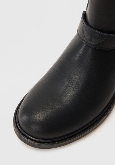 Stivale alla caviglia in pelle nera con punta arrotondata, texture liscia e suola cucita. Presenta una cintura attorno alla caviglia con un sottile dettaglio del logo.