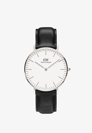 Ronde horloge met een zilveren metalen kast, witte wijzerplaat, dunne zwarte uurmarkeringen en een zwarte leren band. Beschikt over een minimalistisch ontwerp.