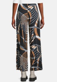 Breda byxor med abstrakta bruna, grå, vita och svarta geometriska mönster, bärs med vita ankelstövlar och en vit topp.