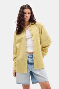 Żółta koszula w kratkę z guziczkami, wykonana z lekkiego materiału, zestawiona z jasnoniebieskimi szortami dżinsowymi o postrzępionych brzegach.