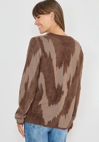 Bruine gebreide trui met een fuzzy textuur. Heeft een ronde hals en lange mouwen, met lichterbruine zigzagmotieven op een donkerdere achtergrond.