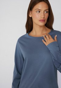 Langarm, ronde hals top van zacht, diepblauwe stof met een gladde textuur. Heeft een relaxed fit en minimale details.
