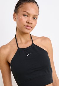 Black halter crop top made of stretchy fabric, features a ruffled neckline and a small white Nike logo on the front.