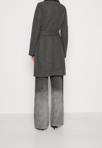 Harmaa villasekoitepäällystakki, jossa on vyötärövyö, lovikaulus ja pitkät hihat, yhdistetty leveälahkeisiin harmaisiin liukuvärifarkkuihin.