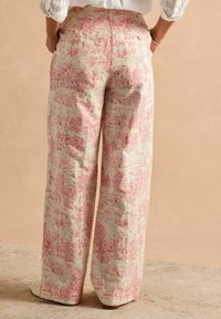 Nohavice s širokými nohavicami v ružovo-krémovom kvetinovom vzore, vyrobené z mäkkej tkaniny s textúrovaným povrchom. Majú zadné vrecká a voľný strih.