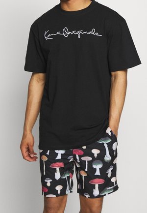 Czarna bawełniana koszulka z białym, pisaną czcionką logo. W połączeniu z czarnymi szortami z kolorowym nadrukiem grzybów. Szczegółowy design i luźny krój.