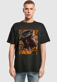 Camiseta de algodón negra con un gráfico naranja de un diseño de perfil coronado. Corte relajado con mangas cortas y cuello redondo.