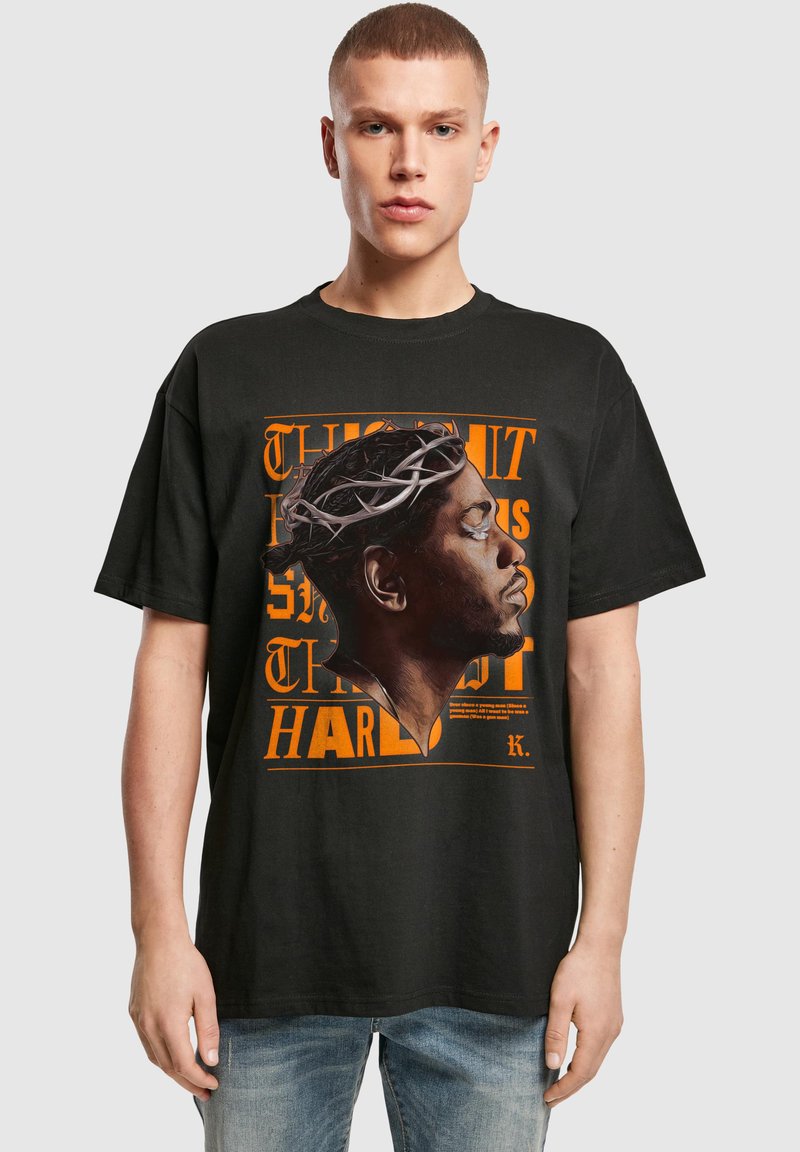 Camiseta de algodón negra con un gráfico naranja de un diseño de perfil coronado. Corte relajado con mangas cortas y cuello redondo.