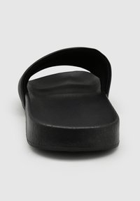 Zwarte slip-onsandalen met een brede, gebogen band en een platte, gestructureerde zool, met een minimalistisch ontwerp en duurzaam materiaal.