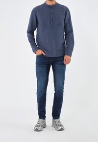 Camicetta blu scuro a maniche lunghe con colletto a bottoni, abbinata a jeans in denim blu e scarpe da ginnastica grigie con finitura testurizzata e dettagli in rete.