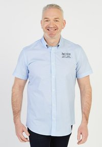 Chemise à manches courtes, bleu clair, avec un micro-motif. Présente un logo sur la poitrine gauche et des poignets boutonnés. Texture du tissu lisse.