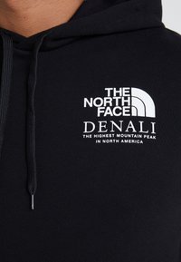 Felpa nera con cappuccio e cordini, con un logo ricamato bianco "The North Face" e il testo "Denali" sul petto.