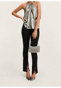 Top halter metálico plateado con tela drapeada, combinado con pantalones negros ajustados con aberturas laterales y un pequeño bolso de cuadros. Los tacones plateados completan el look.