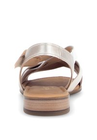 Sandalo con cinturini metallici argento e un accento bianco, dotato di una soletta imbottita color nocciola e un tacco basso marrone.
