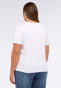 Witte katoenen t-shirt met korte mouwen, ronde halslijn en een relaxte pasvorm. Gedragen met een blauwe denim broek. Achteraanzicht toont een gladde textuur.