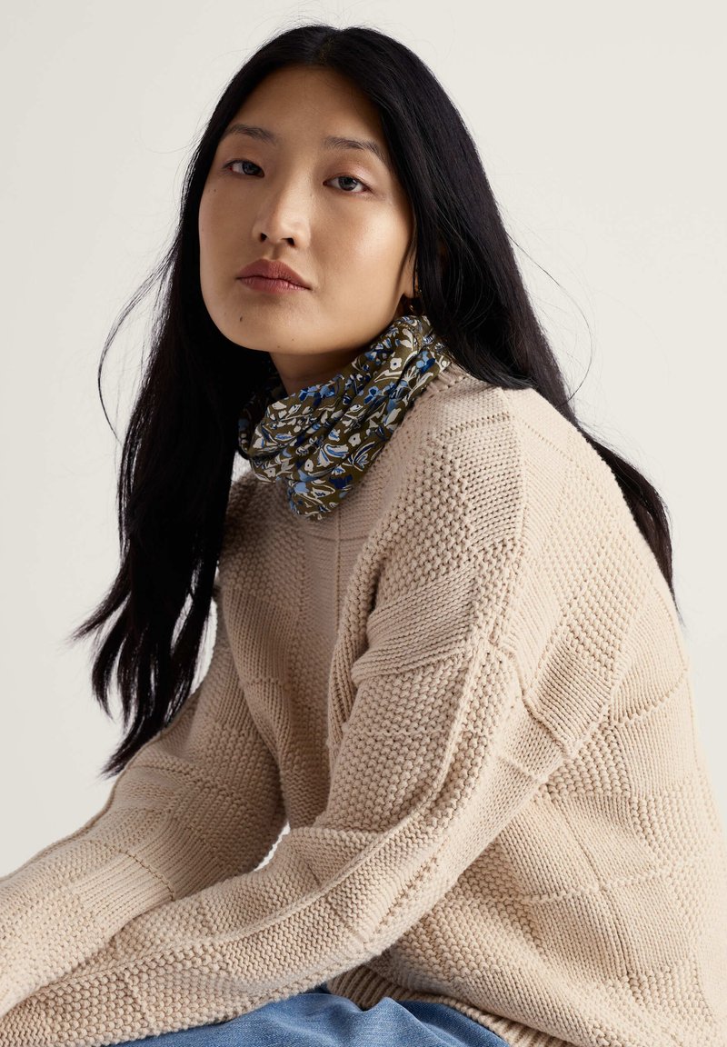 Beežist kootud džemper tekstuurse mustriga, kombineeritud rohelise lillemustriga kaelasalliga, millel on sinised aktsendid. Pehmed materjalid ja lõdvestunud lõige.