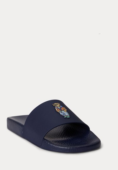 Σ navy μπλε σανδάλι με ανάγλυφη σόλα και μικρή κεντημένη αρκούδα που φοράει καθημερινά ρούχα στο λουρί.