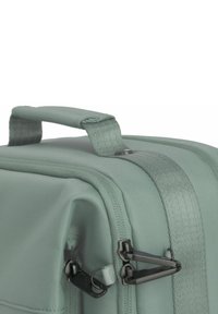 Zaino in morbido tessuto verde con una maniglia robusta, zip nere e superficie testurizzata, progettato per versatilità e durata.