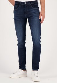 Marinblå skinny jeans i denimtyg med en slät yta, femficksdesign och knappstängning fram, ihop med vita sneakers.