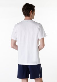 T-shirt bianca in cotone con maniche corte, scollatura rotonda e orlo dritto, abbinata a pantaloni corti blu scuro con una striscia bianca laterale.
