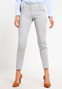 Ljust grå skräddarsydda byxor med en figurnära design, slät textur och sidsömmar. Kombineras med bruna högklackade skor.