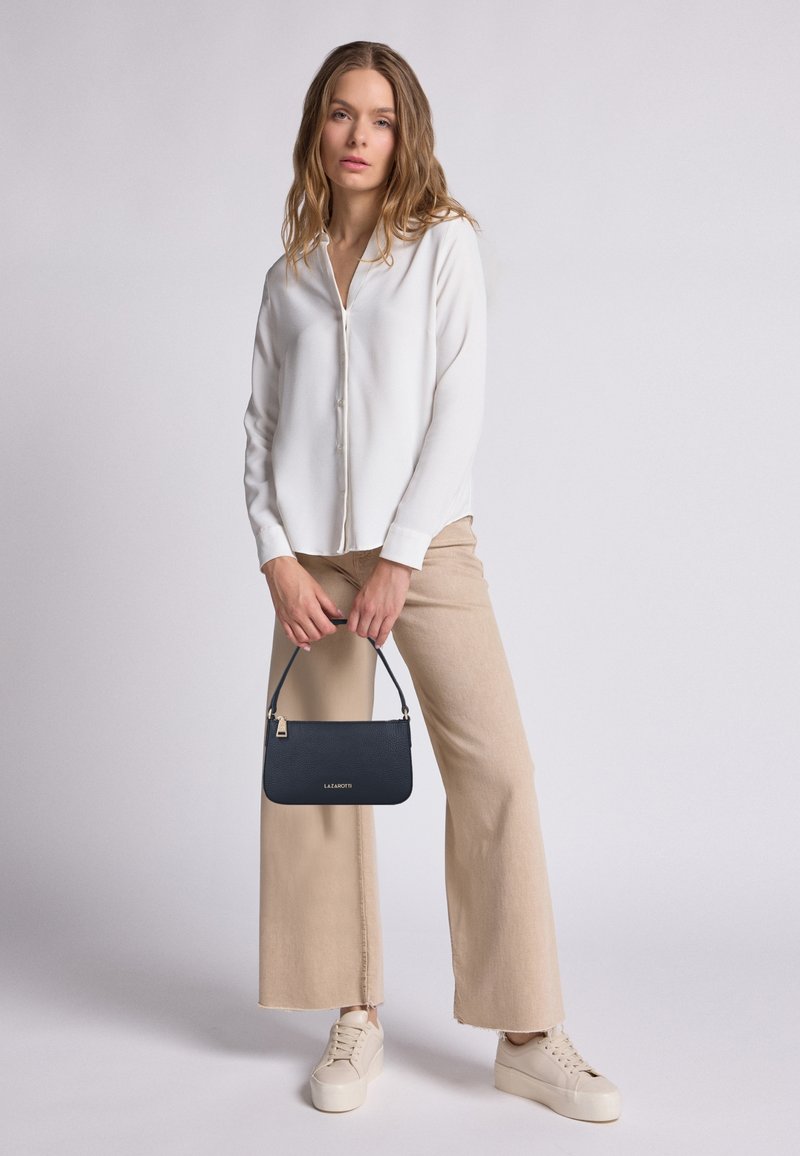 Camisa blanca de botones, pantalones anchos beige, zapatillas de crema y un pequeño bolso azul marino con acabado texturizado y herrajes dorados.