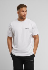 White cotton t-shirt featuring a small black "UPSOCALE" logo on the chest. Short sleeves, relaxed fit, minimal design.