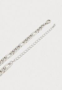 Bracelet en argent avec un design de maillons épais et une fine chaîne à l'extrémité, doté d'un fermoir à mousqueton pour un maintien sécurisé.