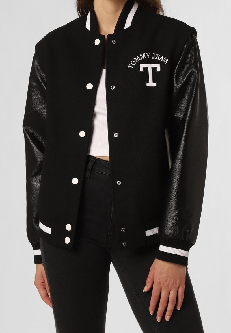 Černá univerzitní bunda s koženými rukávy, bílými knoflíky a vyšívaným logem "T" a "TOMMY JEANS". Hladké manžety a límec s bílými akcenty.