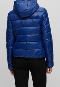 Blå puffjacka med glansig finish, med horisontella quiltade sektioner och en åtsittande huva, kombinerad med ribbade svarta byxor.