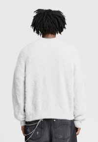 White fuzzy sweater with a relaxed fit, ribbed cuffs, and hem. The back features a soft texture, worn with dark jeans and a silver chain.
