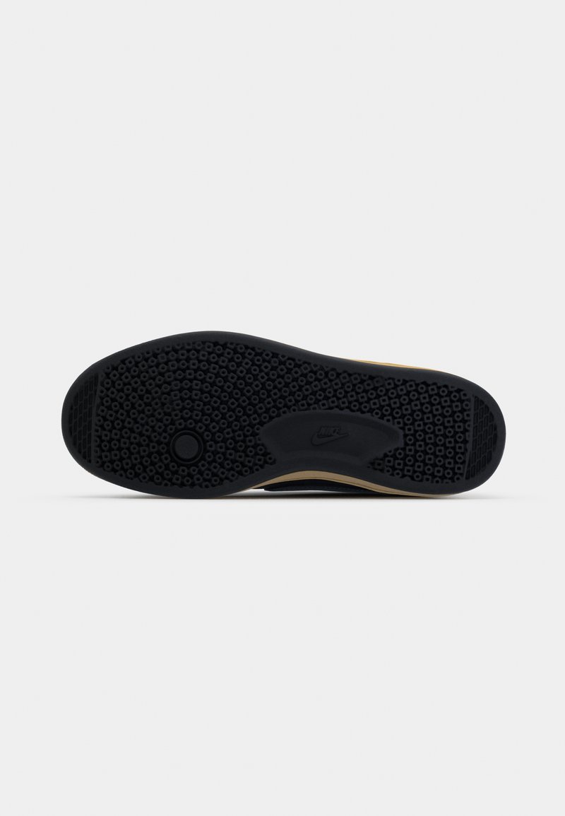 Semelle de sneaker noire en caoutchouc texturé pour une meilleure adhérence, avec un logo circulaire et un bord crème le long du côté.