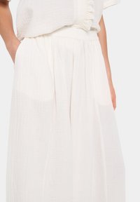 Jupon blanc léger plissé avec une taille élastique. Présente une texture douce et un design fluide, idéal pour un port décontracté.