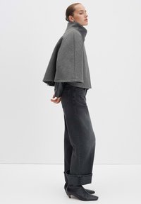 Graue Wolljacke in cropped Schnitt mit hohem Kragen, kombiniert mit dunkelblauen Jeans, die an den Knöcheln umgeschlagen sind, und schwarzen Lederstiefeletten.