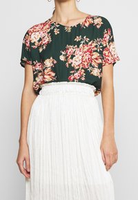 Halenka s krátkým rukávem s tmavě zeleným základem a květinovým vzorem v odstínech růžové a krémové. V kombinaci s bílou skládací sukní.