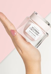 Glass jar of pink cactus pudding skincare product held in a hand, featuring a clear body, silver accents, and a white label with text.